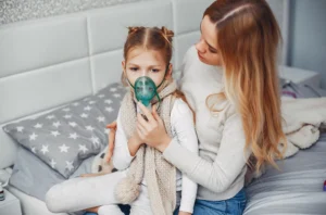 A mother accompanies her daughter, who is wearing an oxygen mask, during a session for asthma evaluation and treatment