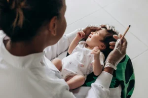 A pediatric healthcare professional prepares to perform an ear piercing on a young infant, ensuring a safe and gentle experience in a medical setting