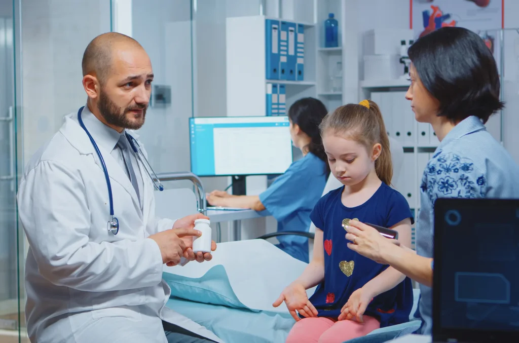 A doctor discusses skin warts treatment with the mother of a young girl in a hospital room, providing care and reassurance.