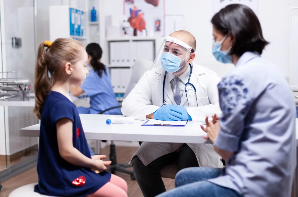 A doctor examines a young girl in a medical office, assessing her skin for warts and discussing treatment options