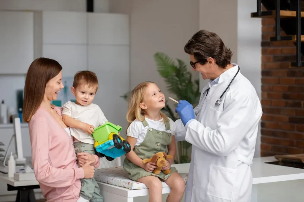 A doctor checks a child with a toy, accompanied by a young mother and her children in the examination room.