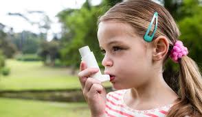 A young girl with light skin and brown hair using an inhaler outdoors, highlighting the prevalence of childhood asthma in New Jersey.